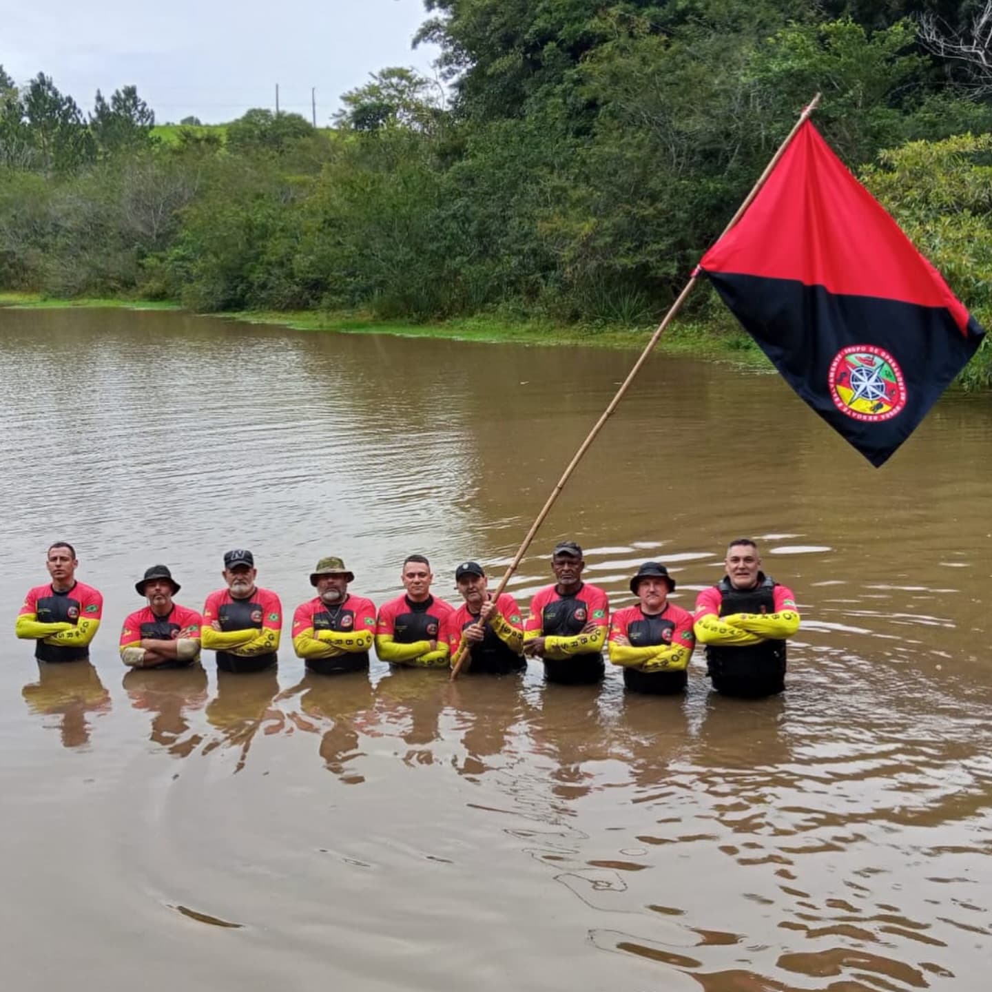 Voluntários do GOBRS perfilados na água durante operação, com a bandeira do grupo